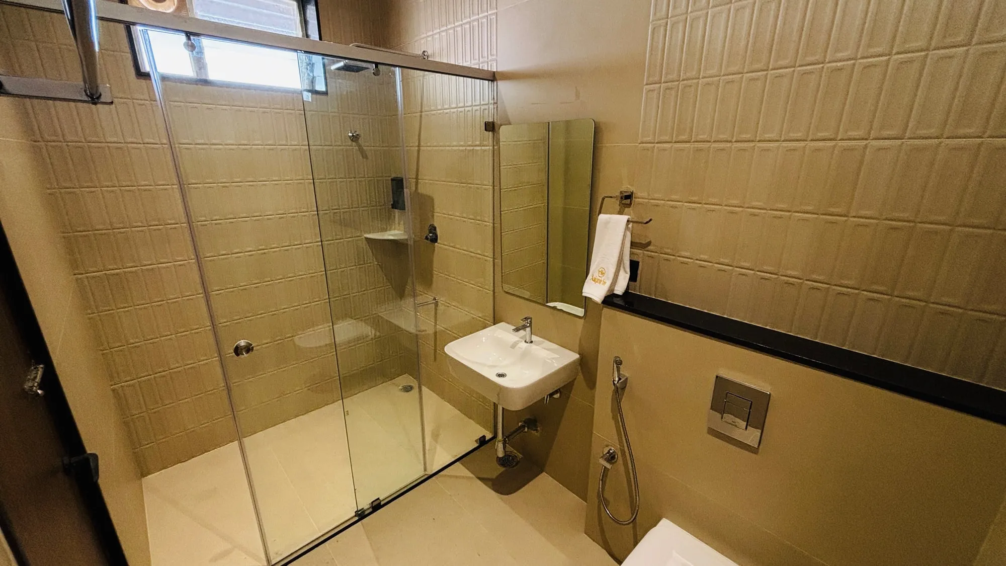 Superior Twin bathroom at Aakarsh Inn in beige tile, with a glass shower cubicle, a wall-hung basin and an Aakarsh Inn towel