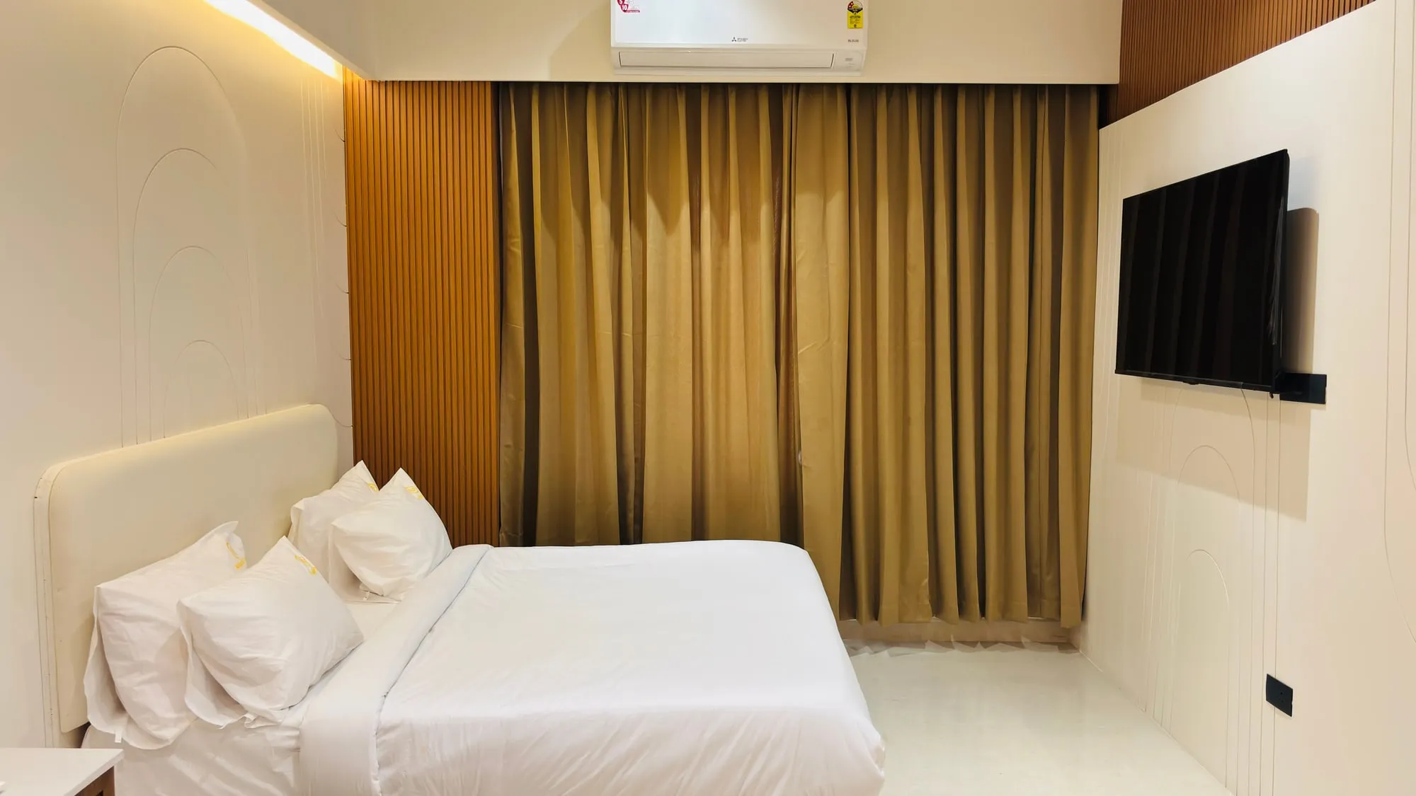 Split air conditioner above drawn curtains and a wall-mounted smart TV in the Suite Room at Aakarsh Inn