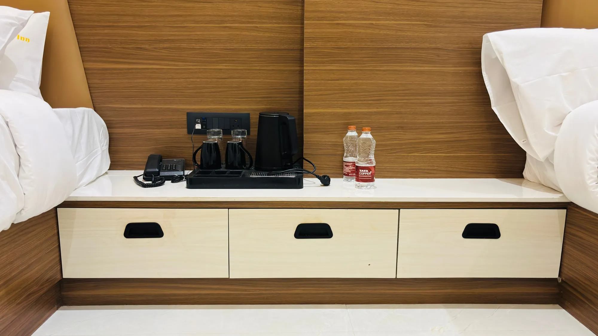 Bedside ledge in the Superior Twin with a kettle, two cups, two glasses, a telephone and two sealed bottles of water